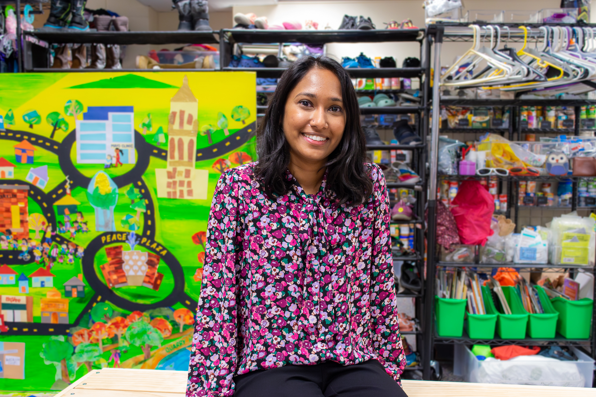 photo of a smiling brown-skinned woman sitting in a colorful room