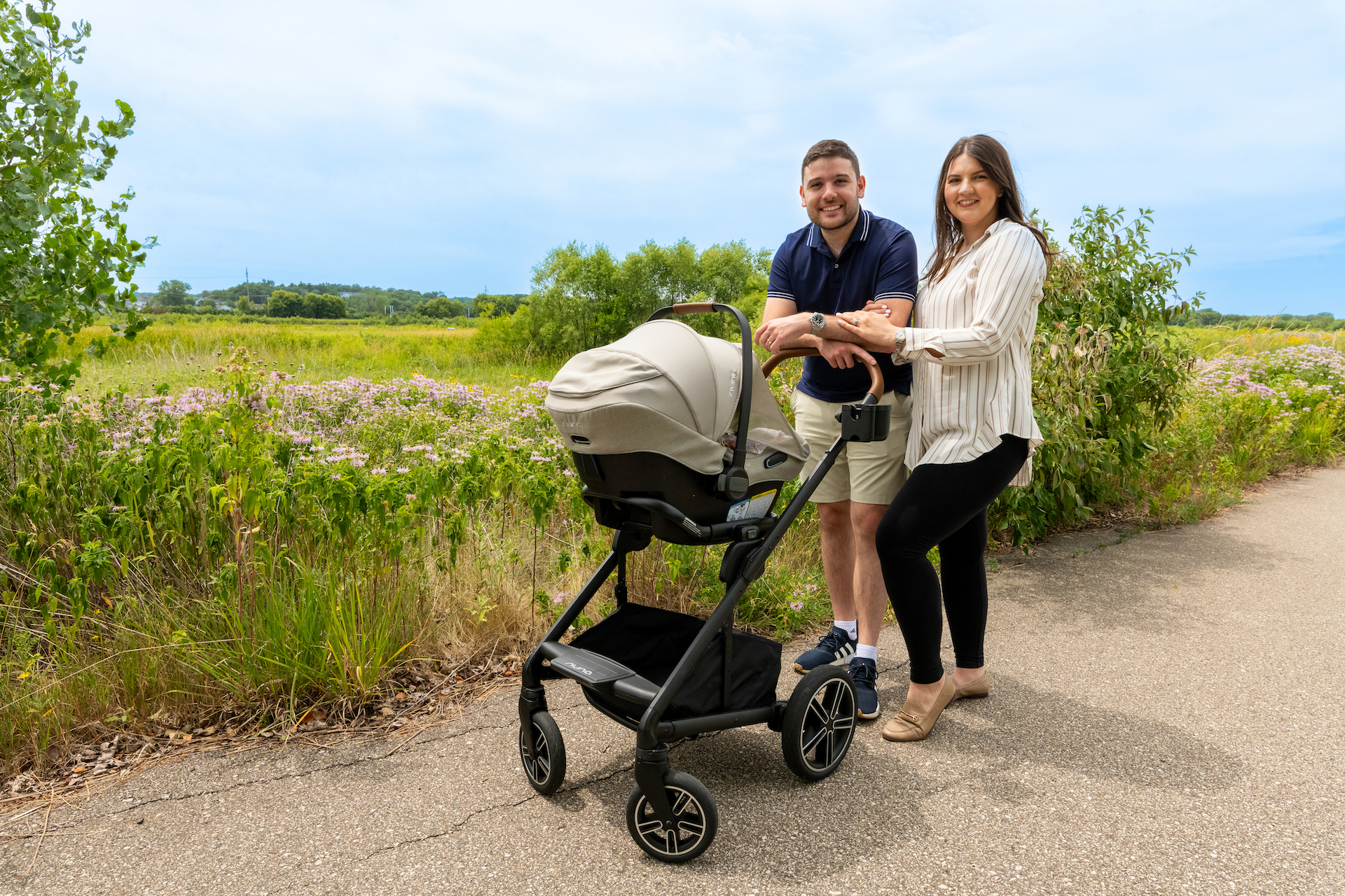 Eastern european husband and wife standing with stroller on path through field of wildflowers