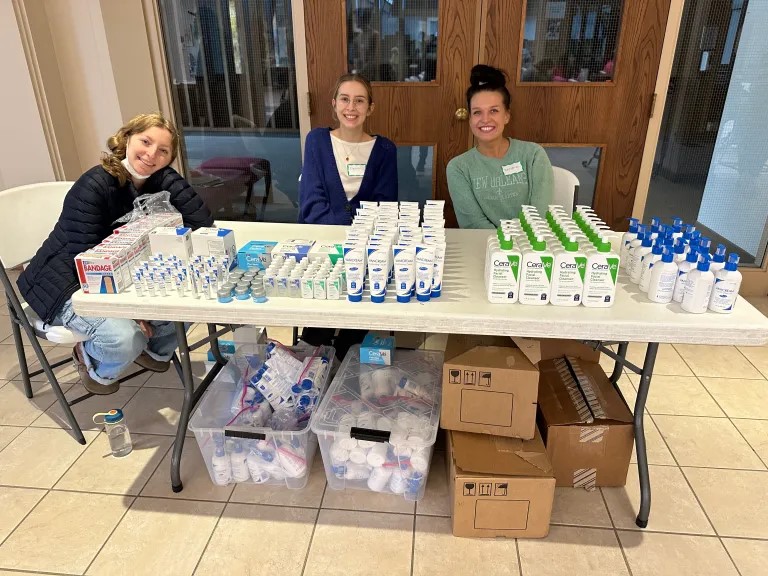 Photo of three white women sitting behind a table full of dermatology products.